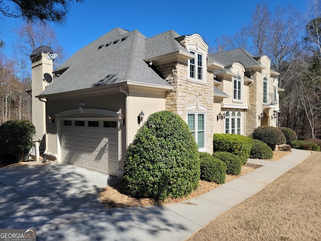 view of home's exterior with driveway, a shingled roof, stone siding, a chimney, and an attached garage