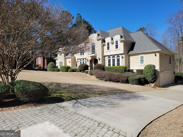 french country home featuring stone siding, concrete driveway, and stucco siding