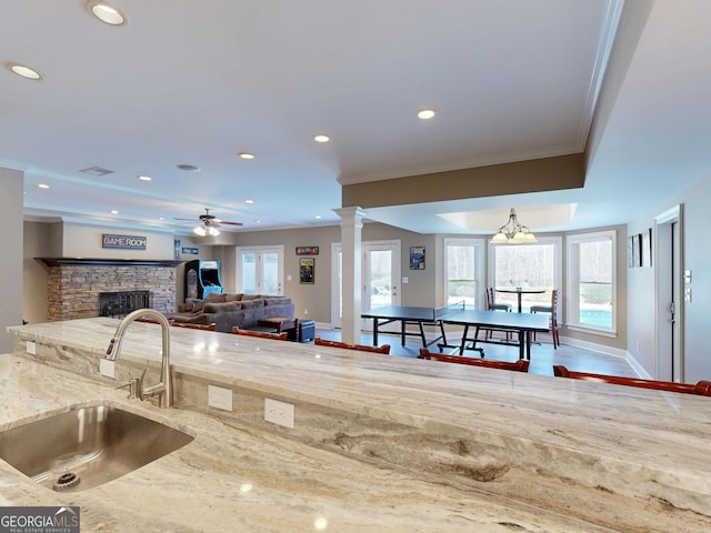 kitchen with ornamental molding, a sink, a stone fireplace, and ornate columns