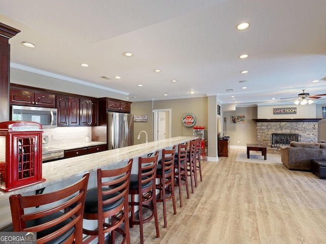 kitchen featuring ornamental molding, stainless steel appliances, a stone fireplace, light wood-style floors, and a kitchen bar