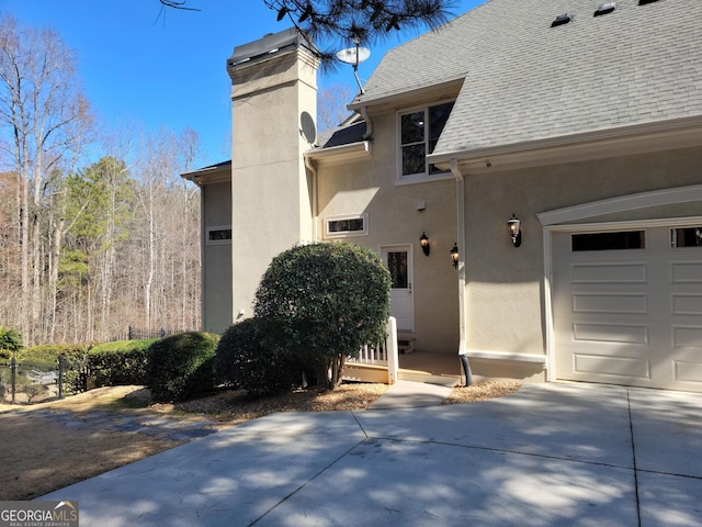 doorway to property with a garage, a shingled roof, driveway, stucco siding, and a chimney