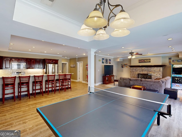 rec room featuring decorative columns, ornamental molding, a stone fireplace, light wood-style floors, and recessed lighting