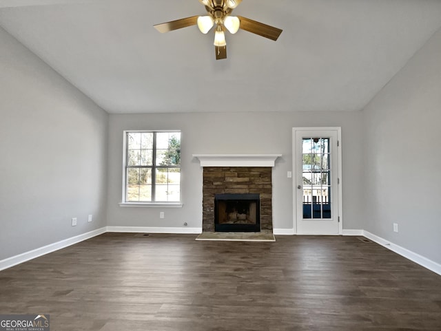 unfurnished living room featuring lofted ceiling, dark hardwood / wood-style floors, a stone fireplace, and ceiling fan