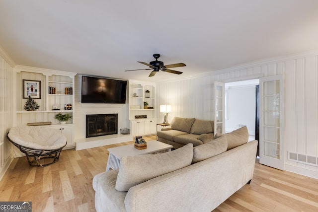 living room featuring ornamental molding, built in shelves, a large fireplace, and light hardwood / wood-style flooring