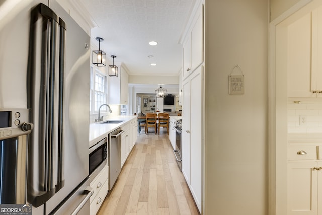 kitchen with appliances with stainless steel finishes, sink, hanging light fixtures, and white cabinets