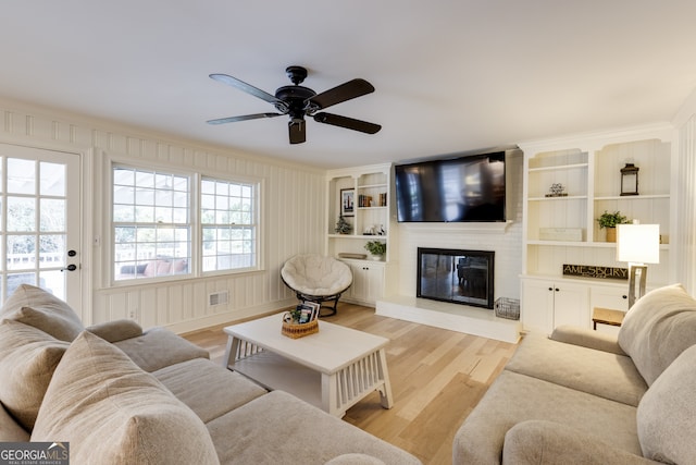 living room featuring ceiling fan, ornamental molding, a large fireplace, and light hardwood / wood-style floors