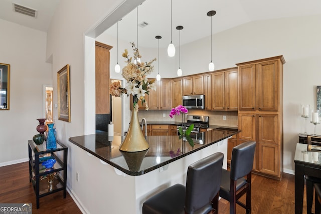 kitchen with dark stone counters, kitchen peninsula, appliances with stainless steel finishes, and a kitchen breakfast bar