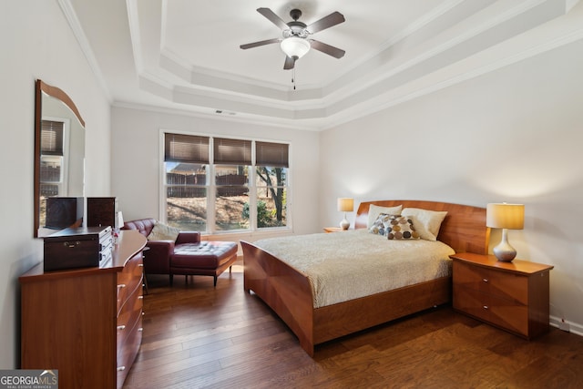 bedroom with a tray ceiling, ornamental molding, dark hardwood / wood-style floors, and ceiling fan