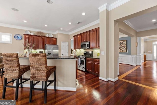 kitchen featuring ornate columns, appliances with stainless steel finishes, dark hardwood / wood-style floors, a breakfast bar area, and ornamental molding