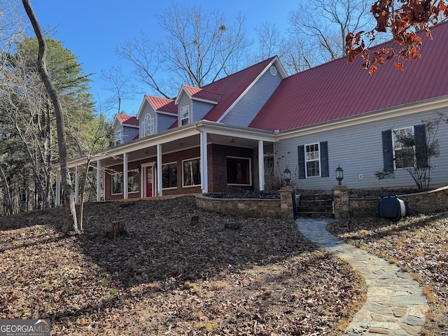 cape cod home featuring brick siding, metal roof, and covered porch