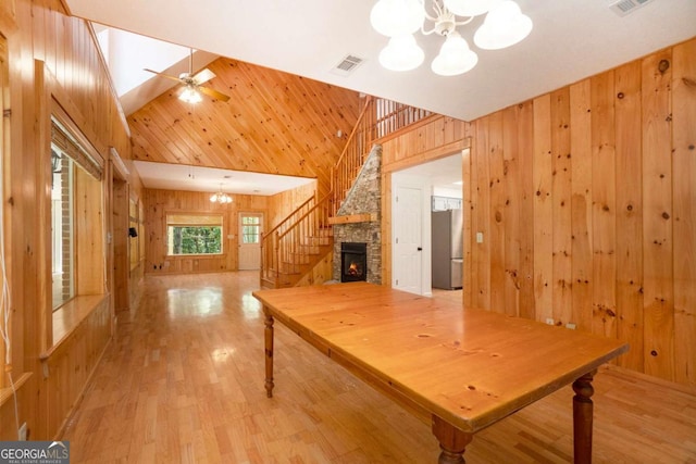 interior space with visible vents, stairs, wooden walls, a stone fireplace, and light wood-type flooring