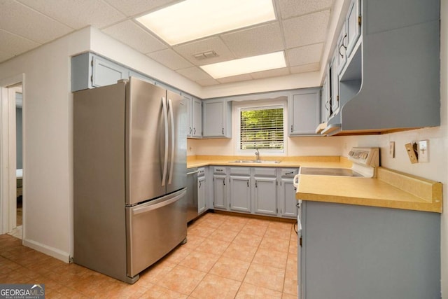 kitchen with appliances with stainless steel finishes, light countertops, a sink, a drop ceiling, and gray cabinetry