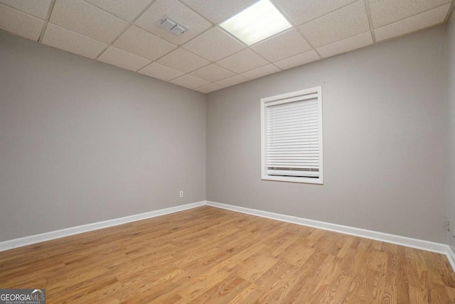 spare room featuring light wood-type flooring, visible vents, baseboards, and a paneled ceiling