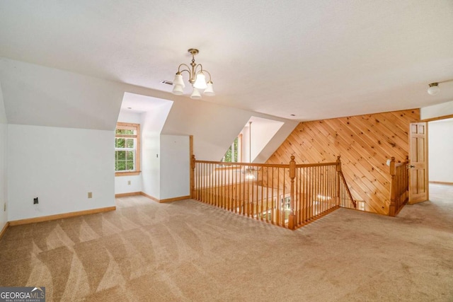 additional living space featuring baseboards, light carpet, lofted ceiling, and wooden walls