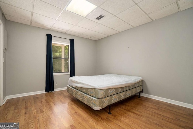 bedroom with baseboards, visible vents, wood finished floors, and a drop ceiling