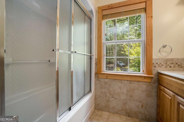 bathroom featuring vanity, tile walls, combined bath / shower with glass door, tile patterned flooring, and wainscoting