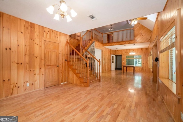 unfurnished living room with a towering ceiling, stairway, wood finished floors, wood walls, and visible vents