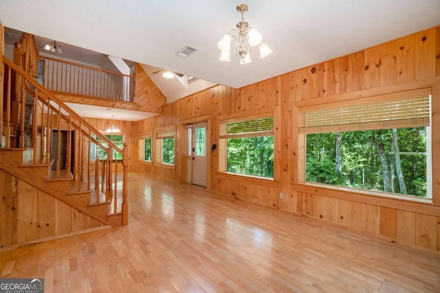 unfurnished living room featuring stairway, wooden walls, visible vents, light wood-style floors, and a notable chandelier