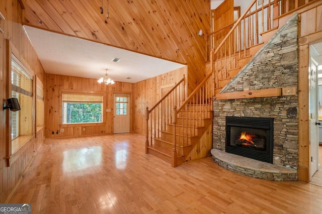 unfurnished living room featuring visible vents, a stone fireplace, wood walls, and light wood-type flooring