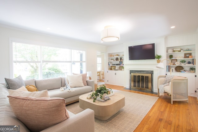 living room featuring hardwood / wood-style floors, crown molding, a fireplace, and built in features