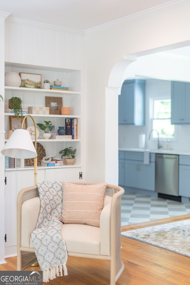 living area featuring built in features, ornamental molding, sink, and light hardwood / wood-style flooring