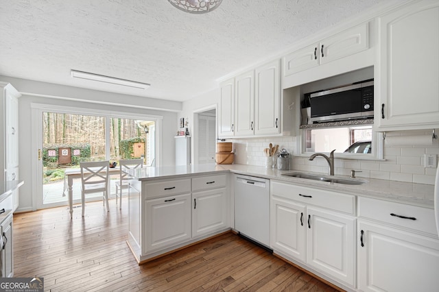 kitchen with sink, dishwasher, kitchen peninsula, light hardwood / wood-style floors, and white cabinets