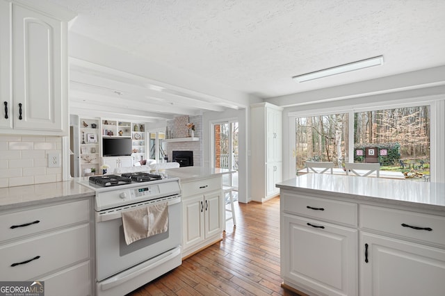 kitchen featuring white cabinetry, white gas range oven, a textured ceiling, a fireplace, and light hardwood / wood-style floors