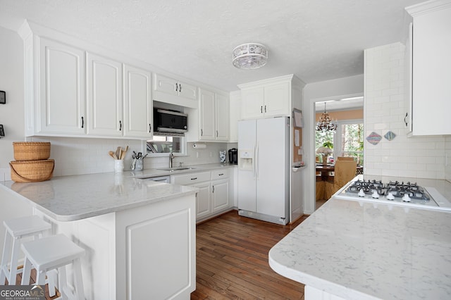 kitchen featuring white cabinetry, gas stovetop, white refrigerator with ice dispenser, light stone countertops, and kitchen peninsula