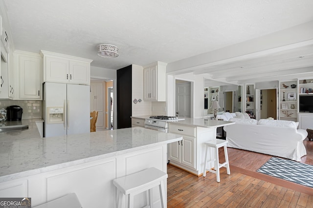 kitchen with a breakfast bar, white cabinetry, white refrigerator with ice dispenser, light stone counters, and kitchen peninsula