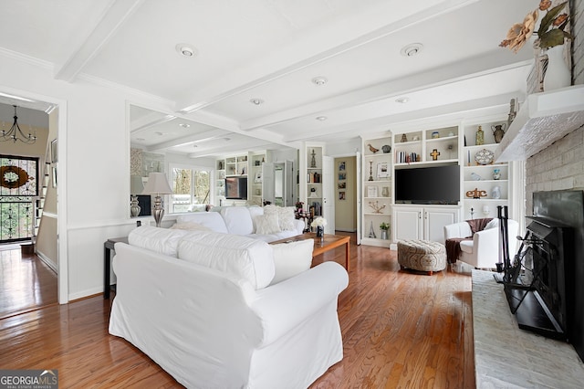 living room with beam ceiling, hardwood / wood-style flooring, an inviting chandelier, and a fireplace