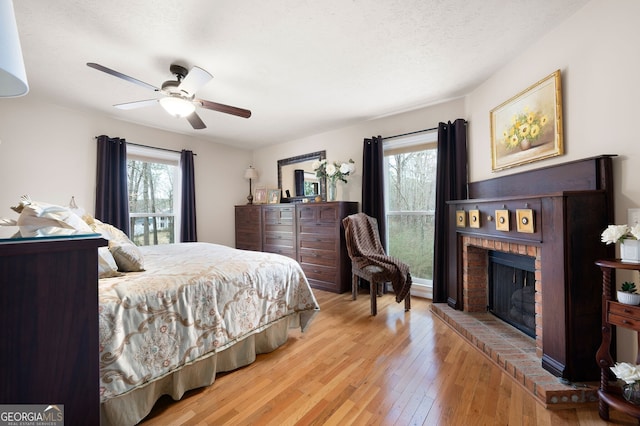 bedroom featuring ceiling fan, light hardwood / wood-style floors, a brick fireplace, and a textured ceiling