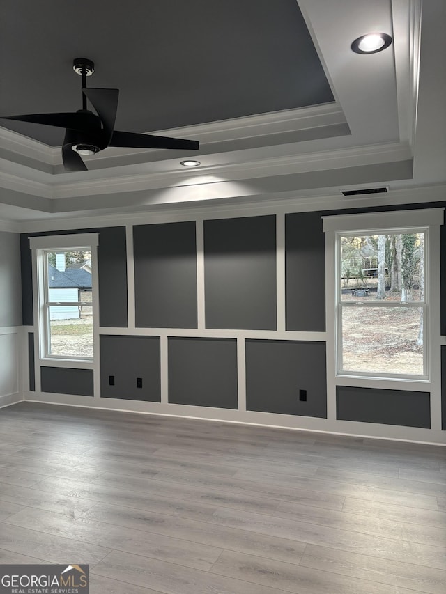 empty room with wood-type flooring, ornamental molding, and a raised ceiling