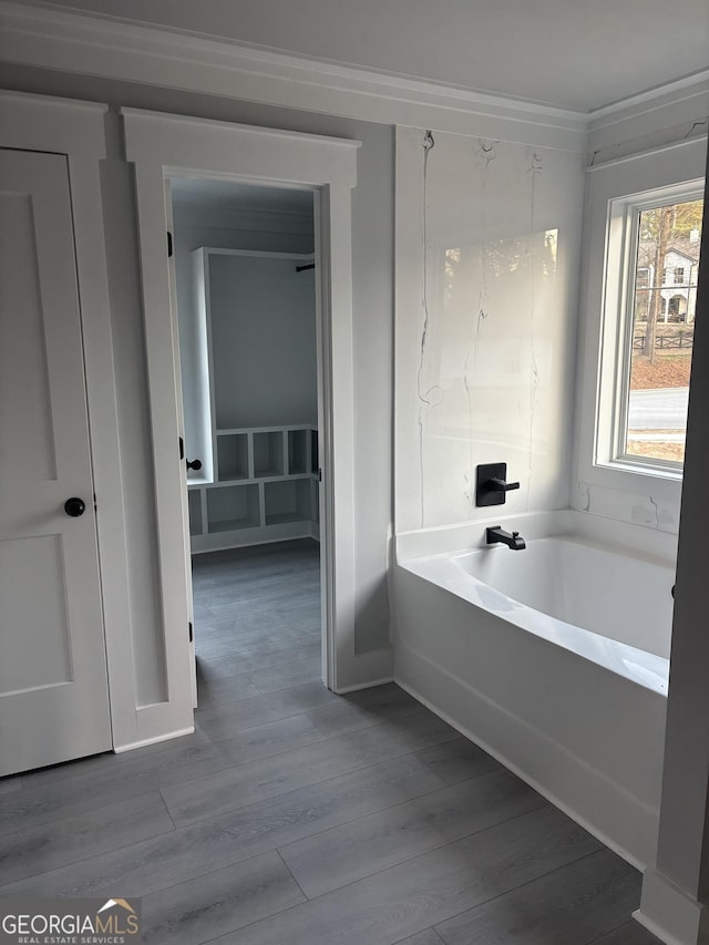 bathroom featuring wood-type flooring, ornamental molding, and a tub to relax in