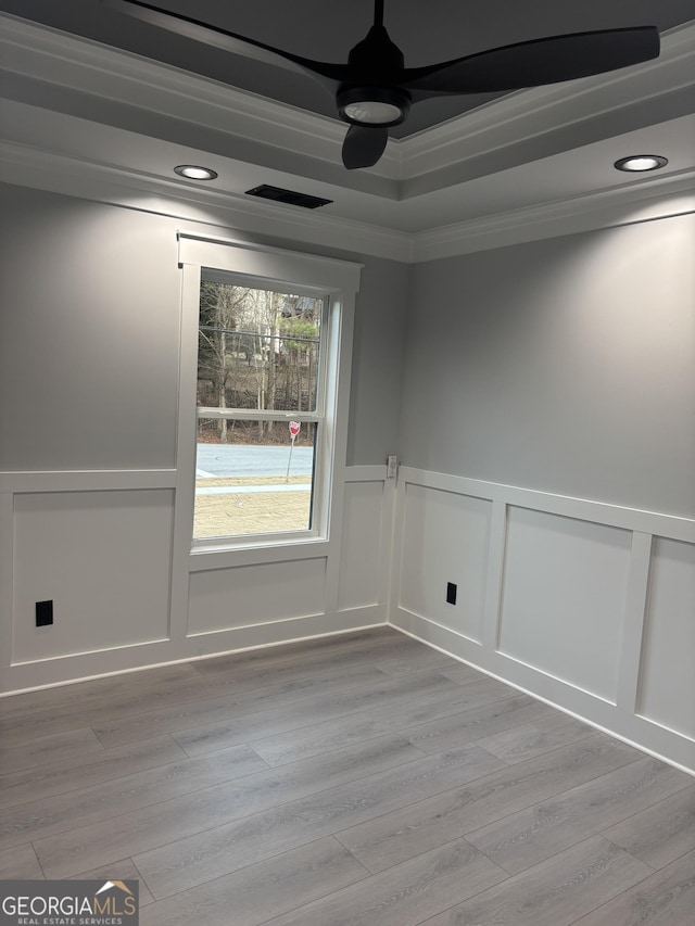 empty room with a raised ceiling, ornamental molding, ceiling fan, and light hardwood / wood-style flooring