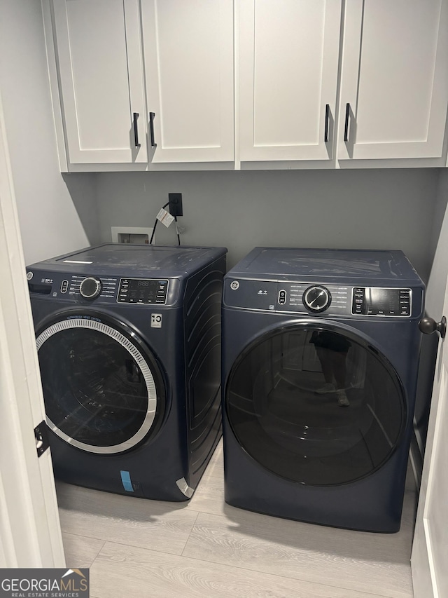 laundry area with cabinets, light wood-type flooring, and washing machine and clothes dryer