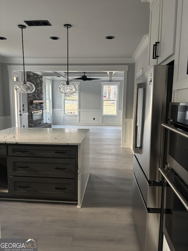 kitchen with crown molding, light stone counters, white cabinets, decorative light fixtures, and high end refrigerator