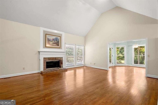 unfurnished living room featuring hardwood / wood-style flooring, ceiling fan, high vaulted ceiling, and a brick fireplace