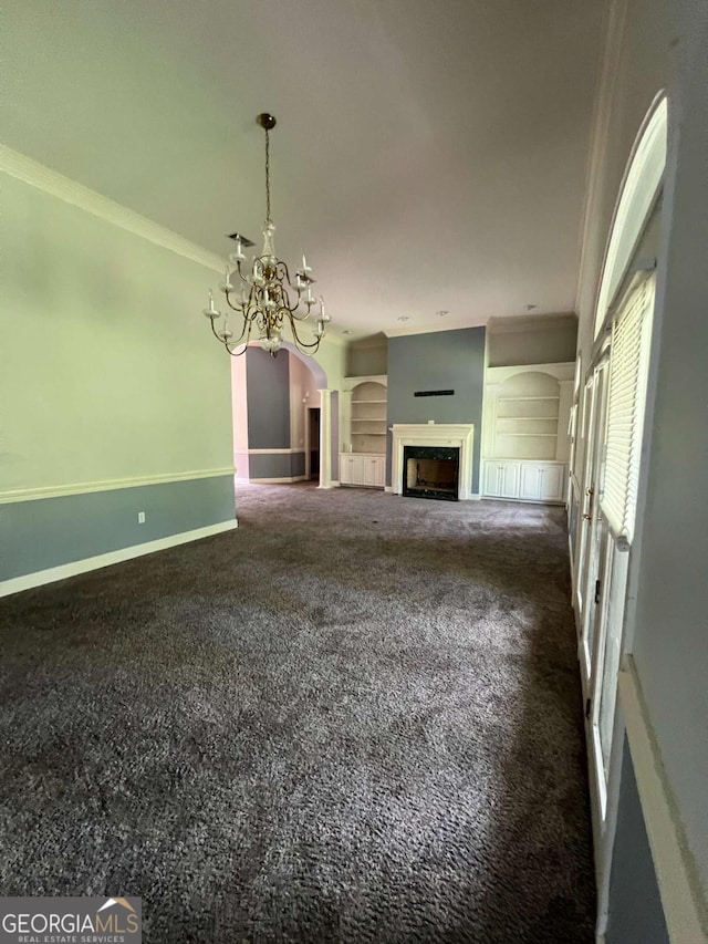 unfurnished living room featuring dark carpet, crown molding, built in features, and a chandelier