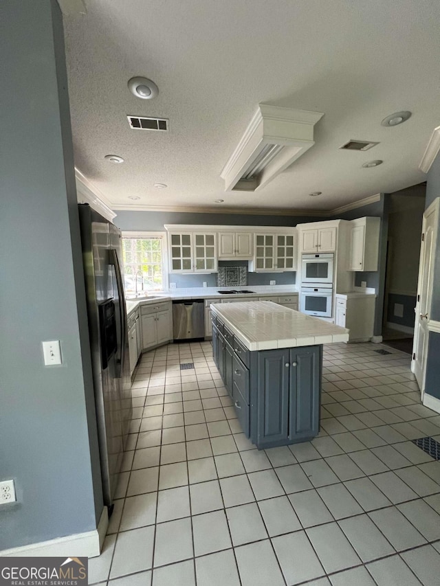 kitchen featuring light tile patterned floors, crown molding, appliances with stainless steel finishes, white cabinetry, and a kitchen island