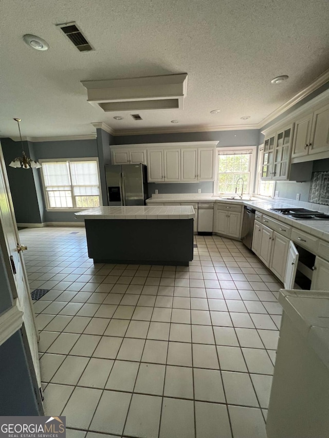 kitchen featuring light tile patterned flooring, sink, hanging light fixtures, ornamental molding, and appliances with stainless steel finishes