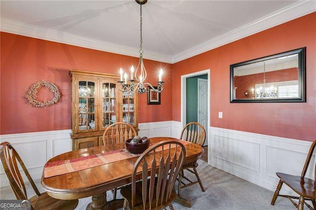 carpeted dining space with an inviting chandelier, ornamental molding, and wainscoting