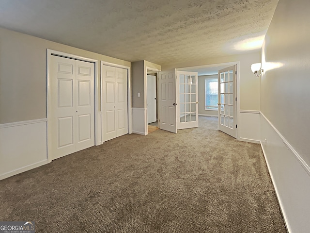 unfurnished bedroom featuring french doors, a textured ceiling, carpet, and two closets