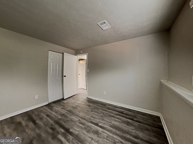 empty room with dark hardwood / wood-style floors and a textured ceiling