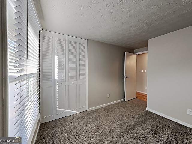 unfurnished bedroom with dark carpet, a closet, and a textured ceiling