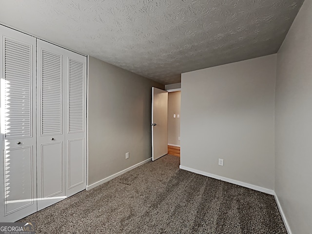 unfurnished bedroom featuring a textured ceiling, dark carpet, and a closet