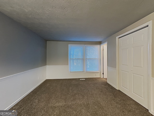 unfurnished bedroom featuring a textured ceiling and dark carpet