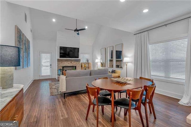 dining room featuring a ceiling fan, baseboards, a brick fireplace, dark wood-style floors, and recessed lighting