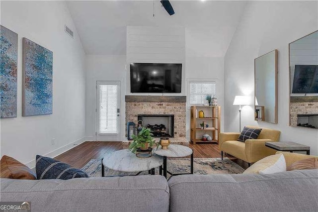 living room featuring wood finished floors, vaulted ceiling, visible vents, and a fireplace with raised hearth