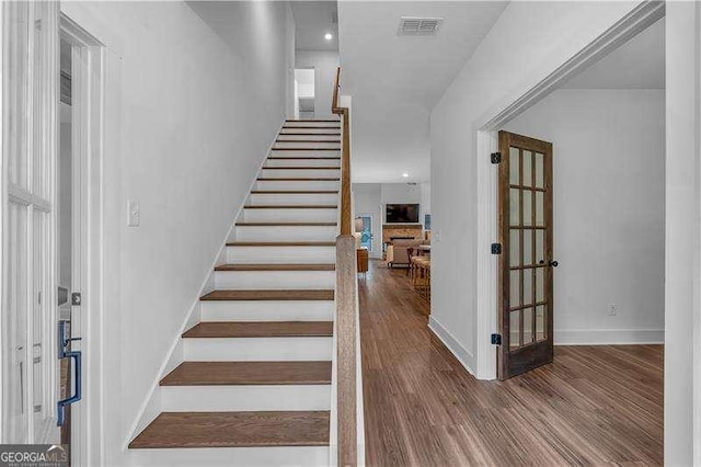 staircase with wood finished floors, visible vents, and baseboards