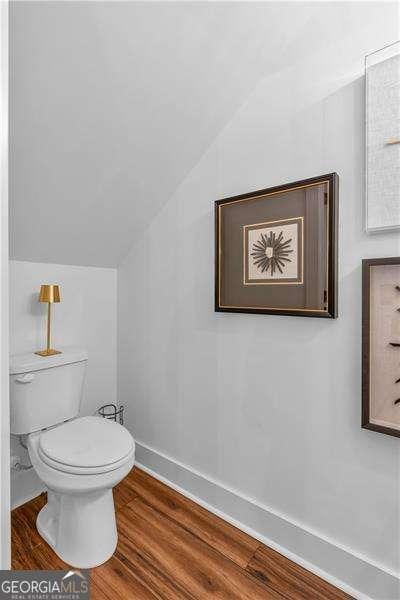 bathroom with vaulted ceiling, toilet, baseboards, and wood finished floors